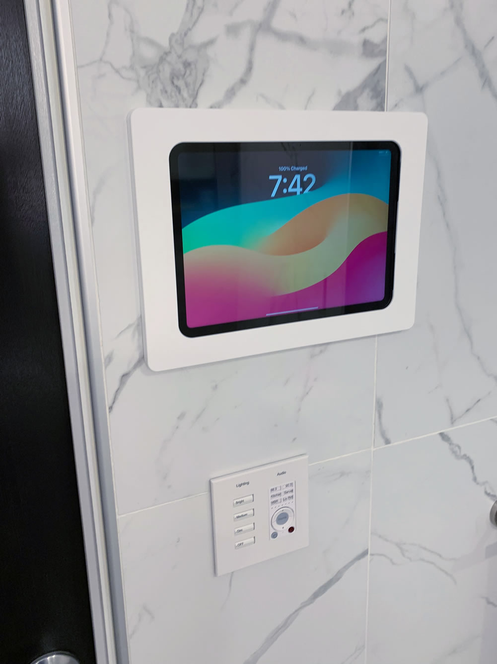 An iPad mounted onto a wall, placed on top of keypad audio controls